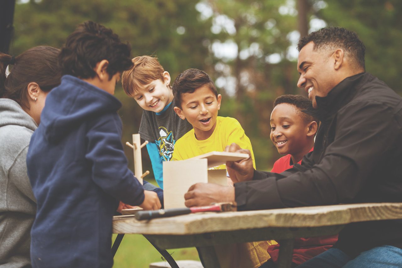 A den works on a project together at an outdoor meeting.