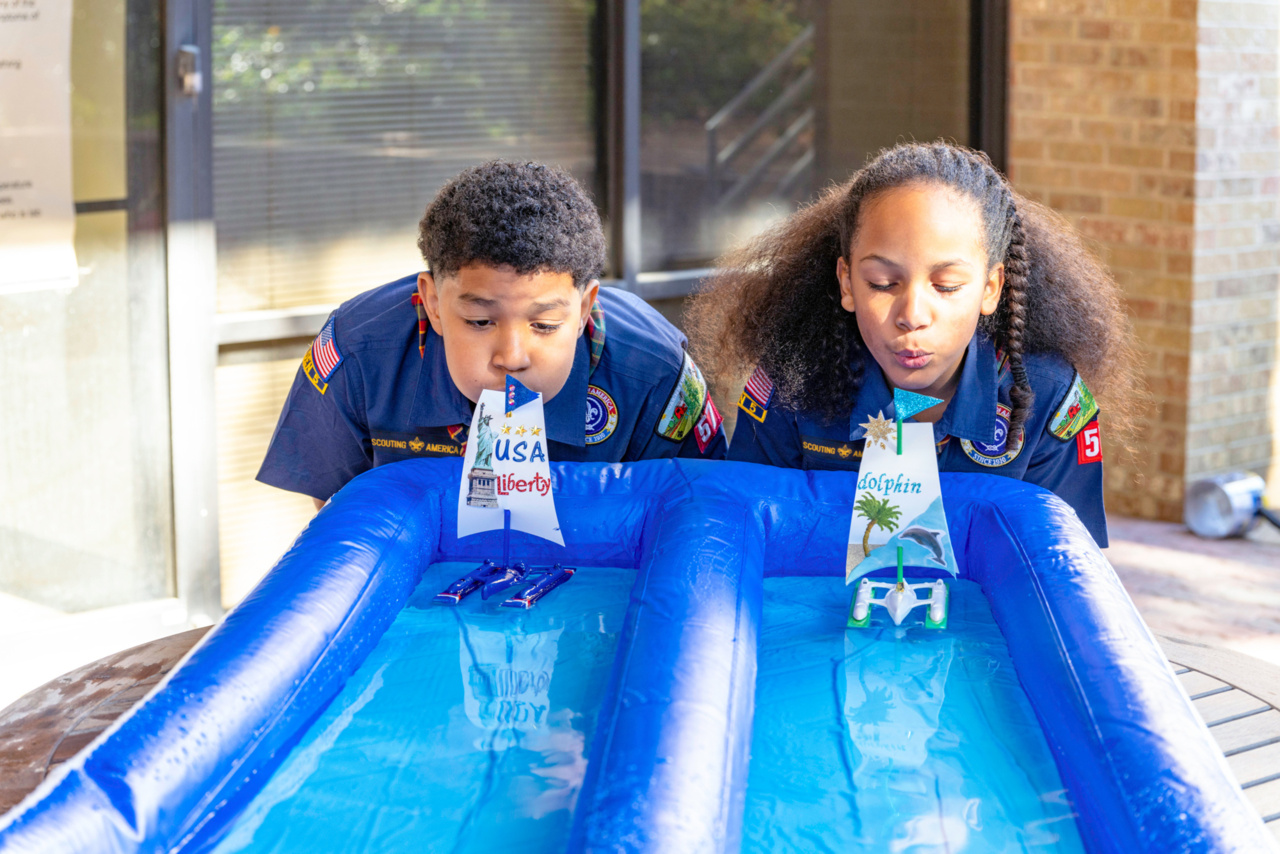 Two cubs blowing on handmade sailboats during a Rain Gutter Regatta.
